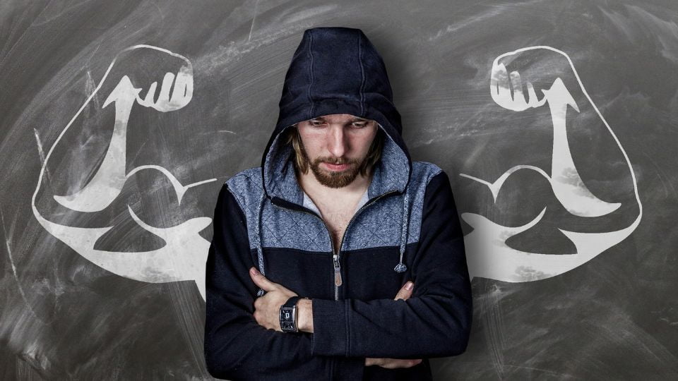 Homem de braços cruzados e roupa de treino com braços musculosos desenhados atrás dele, ilustrando o treino de desenho.