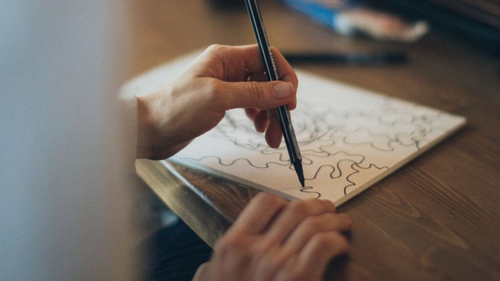 Mãos desenhando com firmeza, ilustrando como ter a mão firme para desenhar.