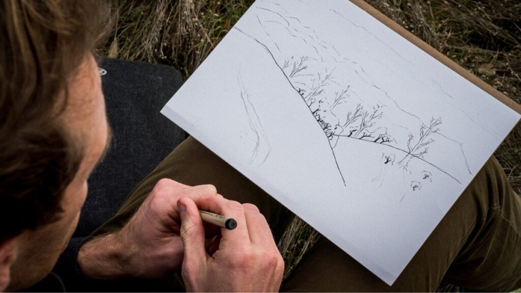 Um homem desenhando uma floresta, ilustrando o que é o desenho a mão livre.