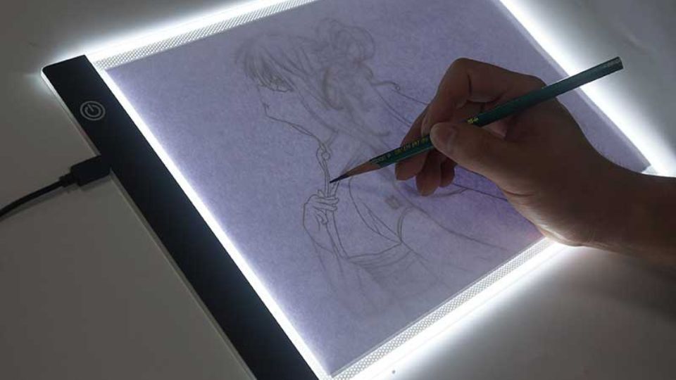 Uma mão segurando um lápis esboçando numa tela iluminada, ilustrando como fazer um esboço com mesa de luz.