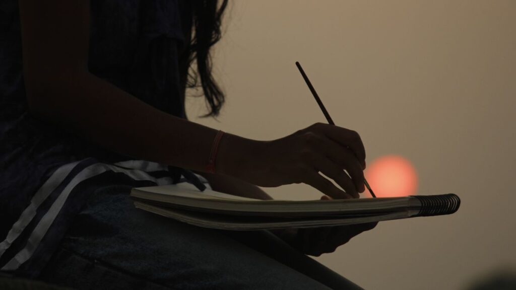 Uma moça desenhando no pôr do sol, ilustrando a sensação de saber como desenhar bem.